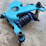 Close-up of a blue coil tattoo machine on a stone surface.