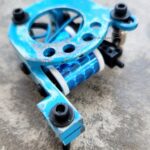 Close-up of a blue mechanical part with bolts on a concrete surface.