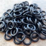 Pile of small black rubber O-rings on a white surface.