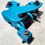 A blue coil tattoo machine on a concrete surface.