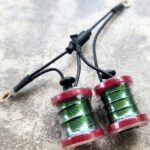 Two red and green fishing reels with attached black cords on a gray surface.
