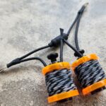 Close-up of a fishing swivel with orange connectors on a concrete surface.