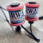 Close-up of two pink fishing bobbers with black tops and labels on a black rod.
