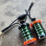Two green coil pickups with orange ends on a concrete surface.