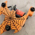 Orange skateboard with a black spider-web design and orange wheels.