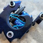 Close-up of a black tattoo machine with blue wires on a gray surface.