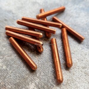 Copper-colored threaded rods scattered on a textured surface.