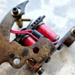 Close-up of a rusty coil tattoo machine on a textured background.