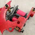 Close-up of a red tattoo machine with coils and springs.
