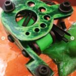 Close-up of a green mechanical part with bolts and holes.