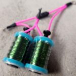 Close-up of green thread spools with pink strings attached.