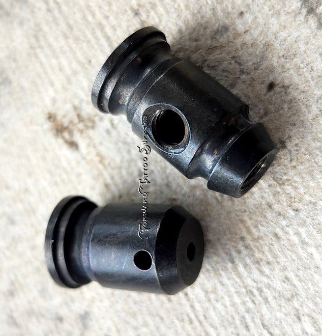 Two black metal parts with holes on a concrete surface.