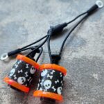 Pair of black and orange earplugs with skull designs on cords.
