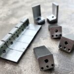 Metal dice and a metal hinge on a surface.