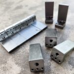 Metal hinge and brackets parts on a concrete surface.