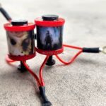 Close-up of a small red and black mechanical device on a concrete surface.