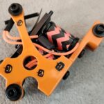 Orange tattoo machine with black grips on a gray surface.