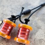 Close-up of two orange fishing line spools with red line on a gray surface.