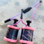 A close-up of two black fishing reels with pink accents and purple lines.