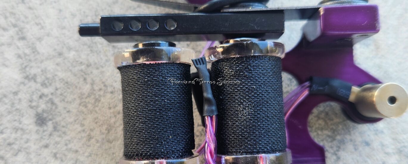 A purple coil tattoo machine on a concrete surface.