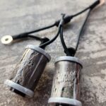 Two small cylindrical objects with strings attached on a wooden surface.