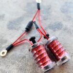 A pair of red electrical coils with wires on a concrete surface.