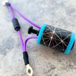 Close-up of a purple wire connected to a blue and black cylindrical electronic component.