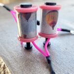 Two small DIY electronic devices with pink wiring on a concrete surface.