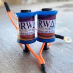 Close-up of two blue electrical coils with orange wires connected.