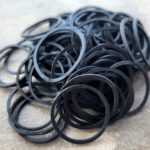 A pile of black rubber O-rings on a surface.