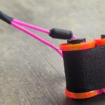 Close-up of a black and pink fishing reel on a gray surface.
