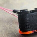 Close-up of a black spool of thread with pink and orange bands on a wooden table.