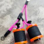 Close-up of tattoo machine coils with pink wires on a textured surface.