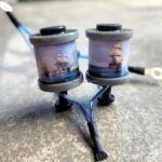 A fishing reel with two spools on a concrete surface.