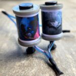 Two tattoo machine coils with dark-themed artwork attached.