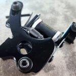 Close-up of a black bicycle derailleur part on a gray surface.
