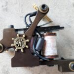 Close-up of a vintage tattoo machine with a ship wheel design.