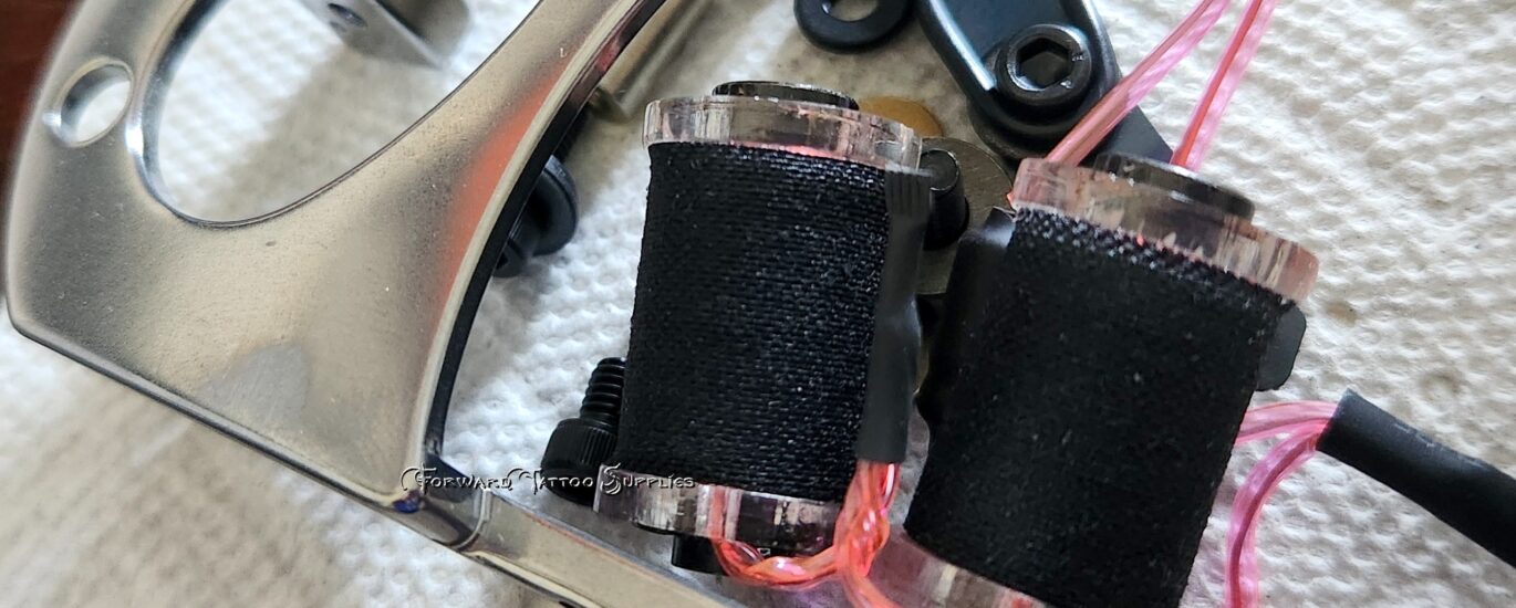 Close-up of a tattoo machine with coils and frame on a cloth surface.