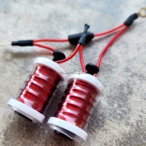 Close-up of two small red and white coils connected by black and red wires.