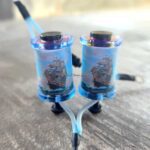 Two blue tattoo machine coils with copper wire wrapped around them.