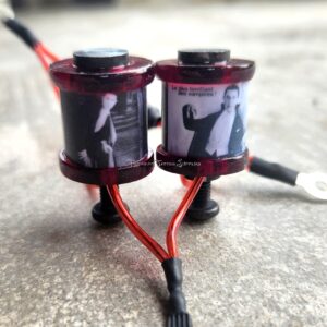 Two small black and red tattoo machines on a concrete surface.