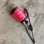A pink and black tattoo machine lying on a concrete surface.