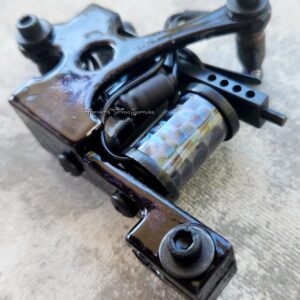 Close-up of a black tattoo machine on a textured surface.