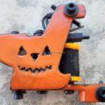 Orange tattoo machine with a Halloween pumpkin face design.
