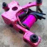 Close-up of a pink tattoo machine with visible coils and screws.