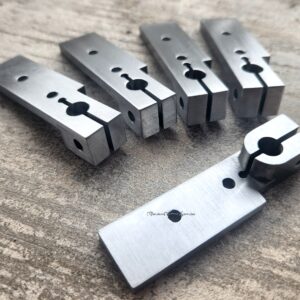 Precision metal parts with drilled holes, arranged on a textured surface.
