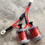 Two red copper wire coils with attached red and black wires on a gray surface.