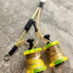 Close-up of two yellow electric buzzers connected by wires on a concrete surface.