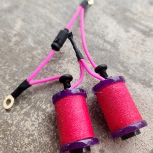 Two spools of pink thread connected by a pink cord on a gray surface.