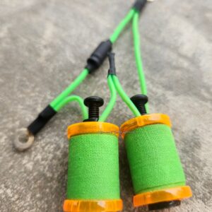 Two green thread spools with threaded needles on a rough surface.